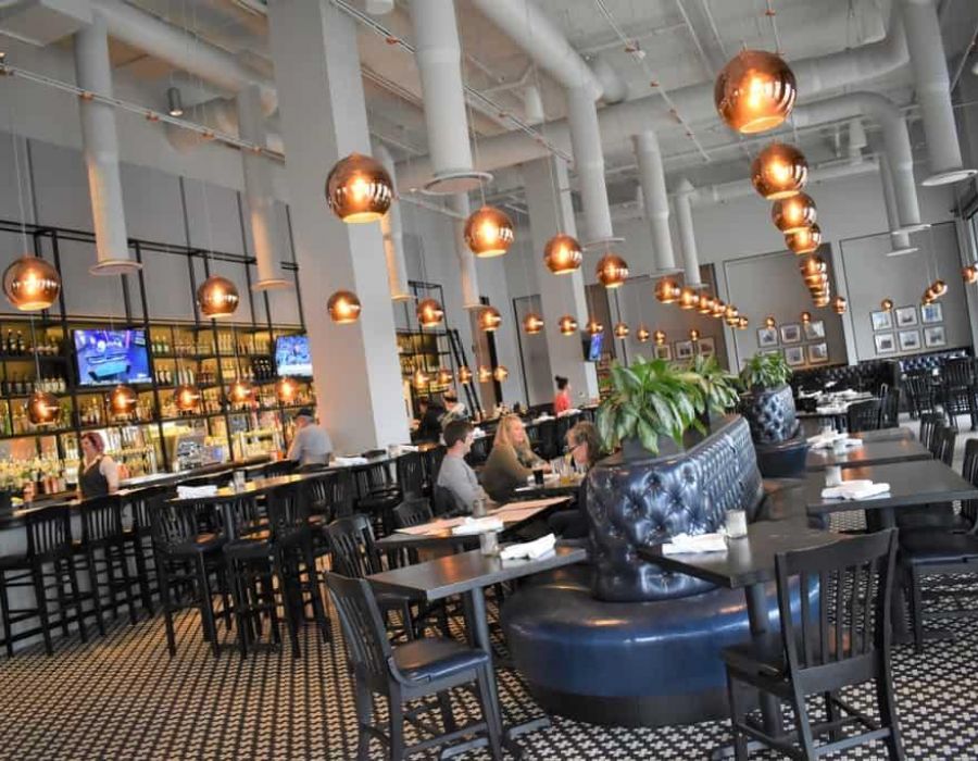 Modern restaurant interior with round hanging lights, tall ceilings, and black tables and chairs, with few people dining.