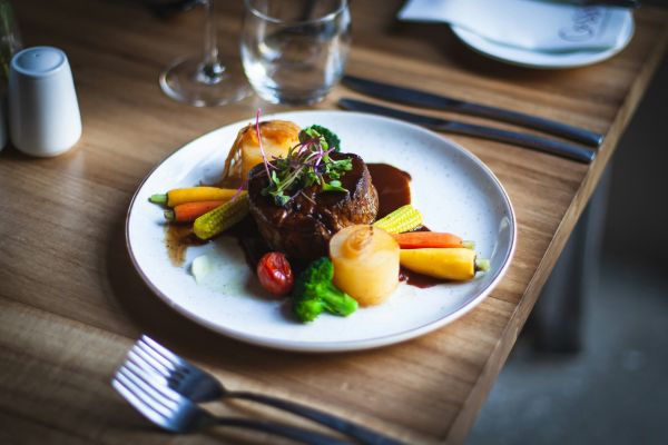 Oberon A plate featuring a serving of meat alongside a colorful assortment of vegetables.