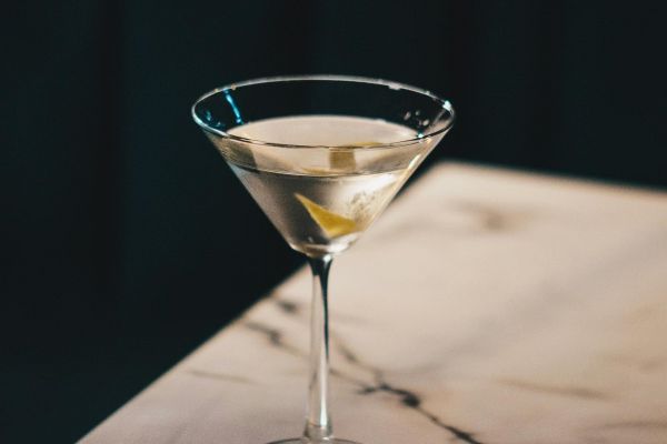 Oberon A martini in a glass sits elegantly on a polished marble table, showcasing its vibrant color and garnished with an olive.